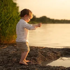 Junge spielt im Kinder Fotoshooting am See mit Steinen