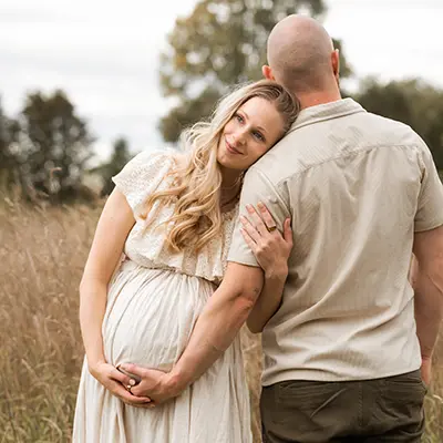 Auf der Wiese steht ein Paar im Schwangerschafts Fotoshooting