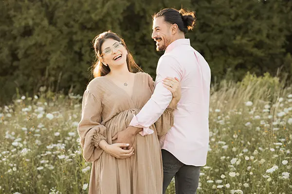 Paar lacht sich im Paar Babybauchshooting auf der Wiese an